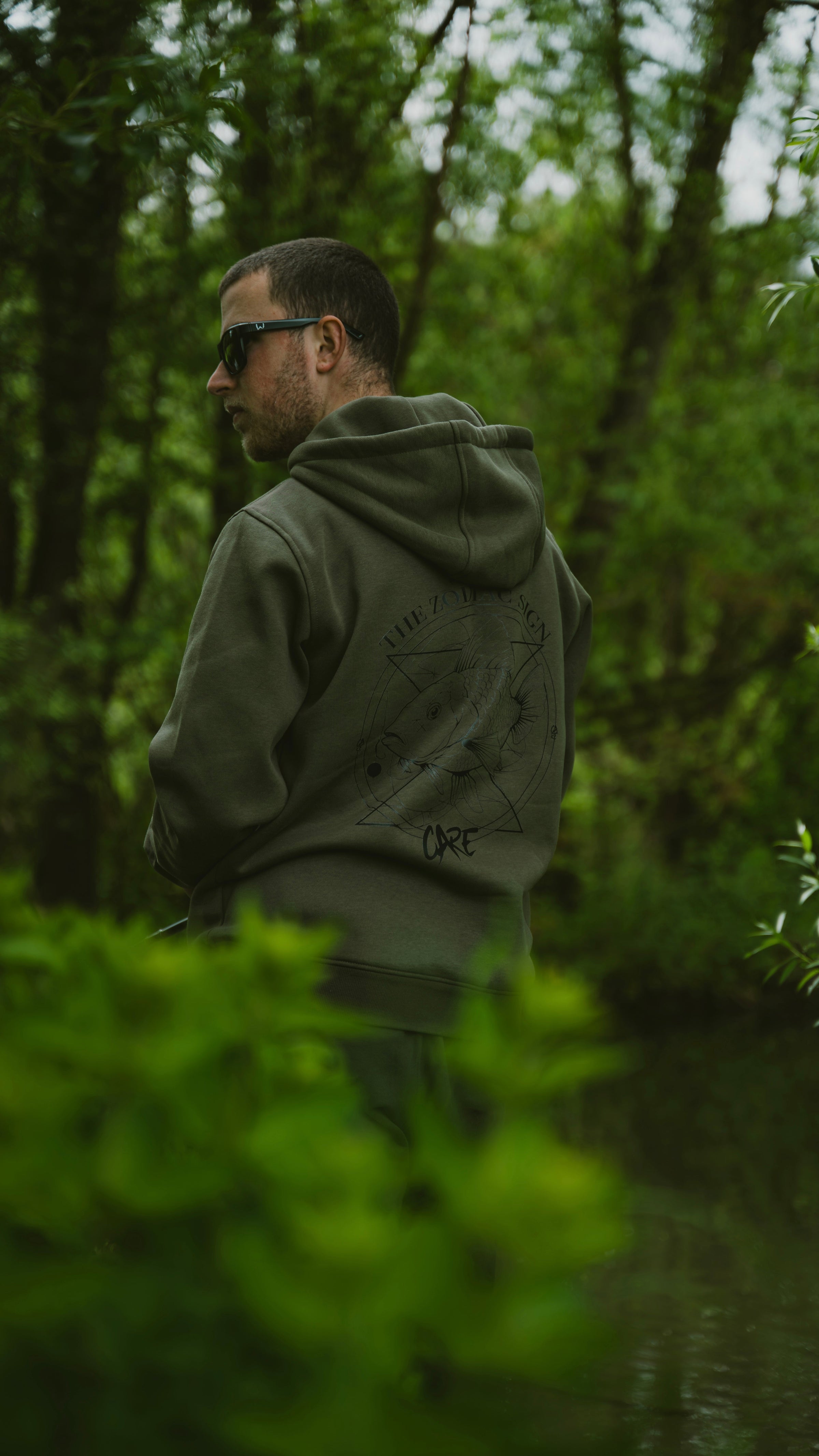 Person in schwarzem CARE Fishing Hoodie mit Libellenmotiv am Wasser