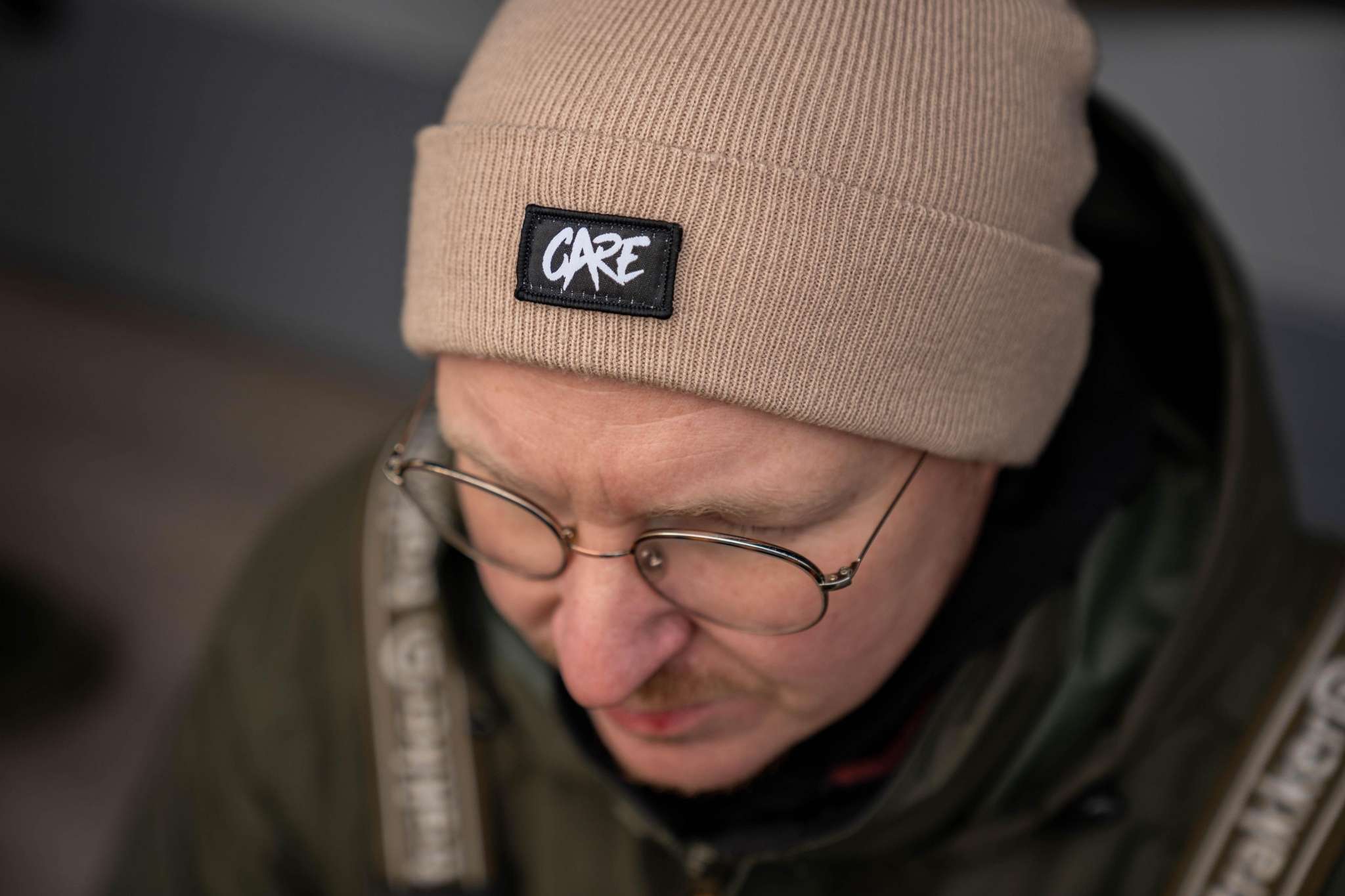 Person mit beigefarbener CARE Beanie und schwarzem Logo-Patch